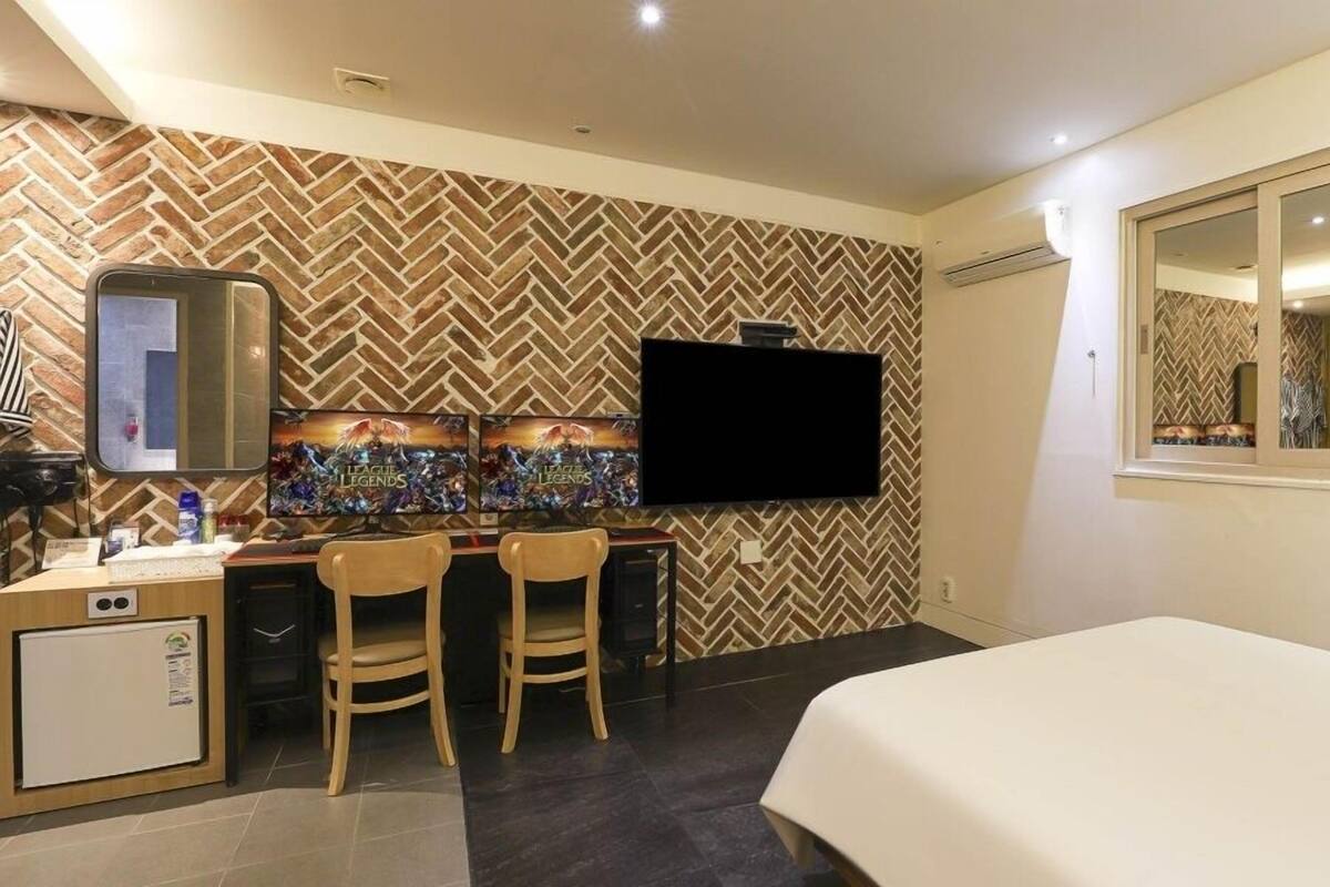 Une chambre d’hôtel avec un mur orné d’un motif en chevrons, un téléviseur à écran plat, un bureau avec deux chaises, un minibar et un lit.