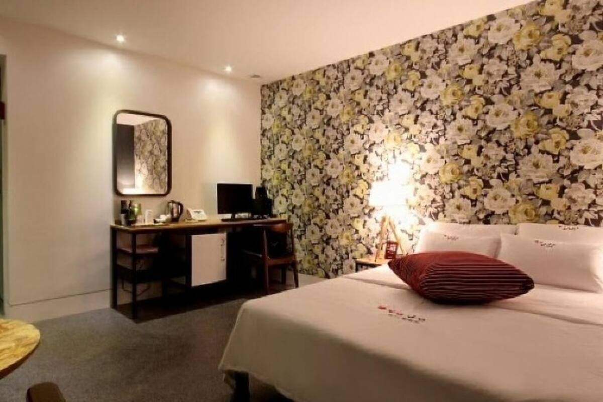 Une chambre d’hôtel avec un lit, un bureau avec un ordinateur, une chaise, une table ronde et un papier peint à motifs floraux.