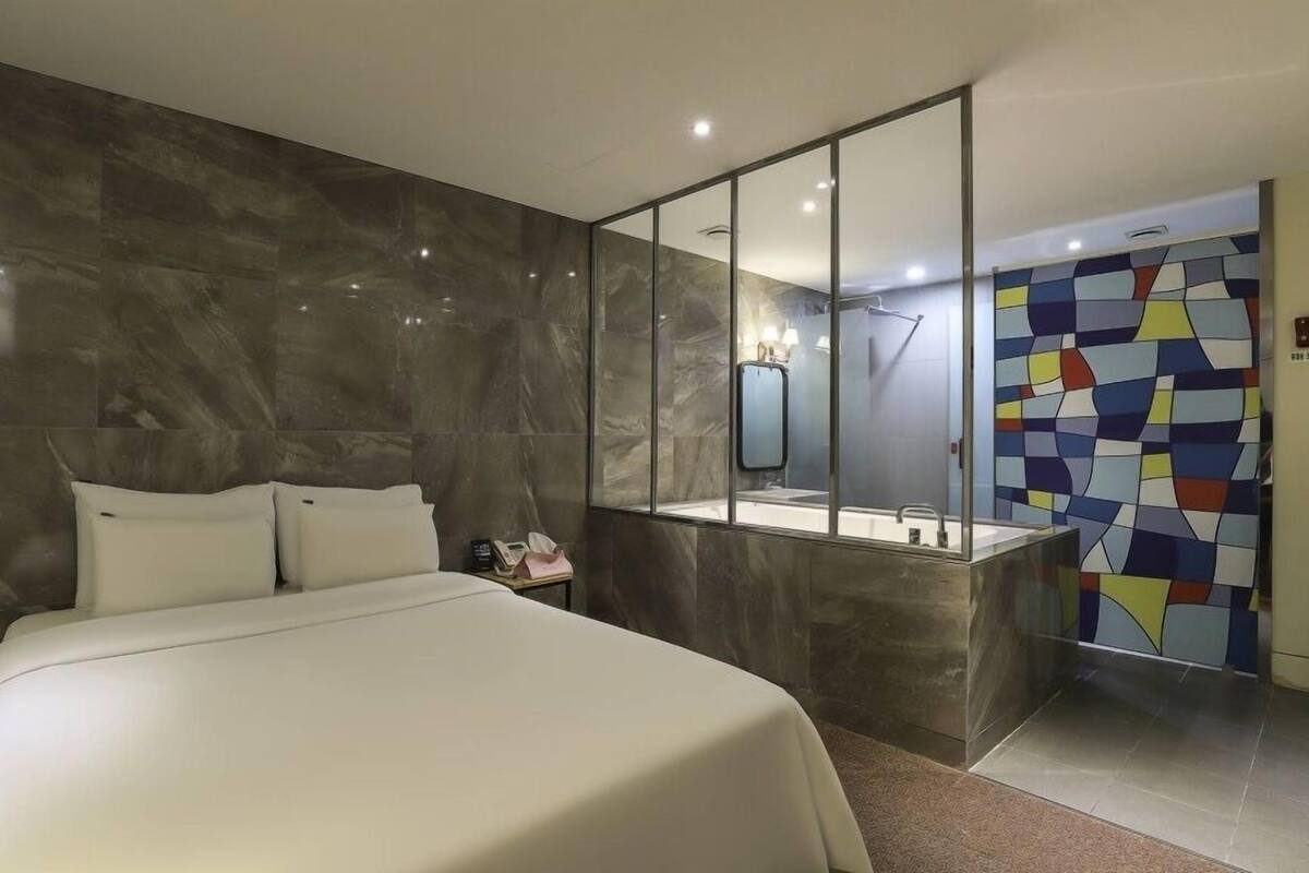 Une chambre d’hôtel moderne avec un grand lit, une salle de bain avec un miroir et un mur décoré de motifs colorés.