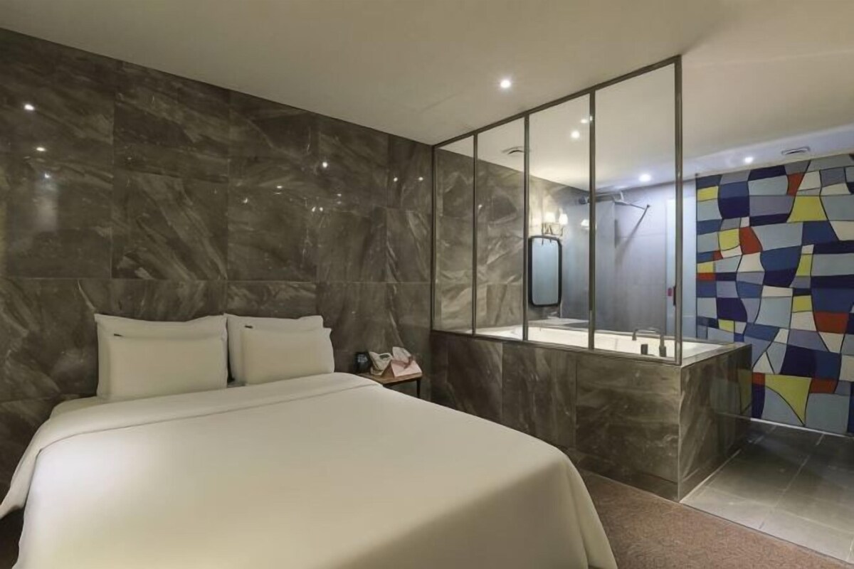 Una habitación de hotel moderna con una cama grande, un baño con espejo y zona de ducha.