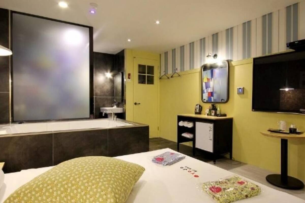 Une chambre d’hôtel avec un grand lit, une salle de bain séparée avec une baignoire, un petit bureau, une télévision et un miroir.