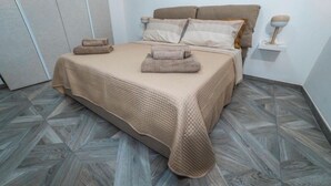 A neatly made bed with a beige bedspread and two folded towels, a bedside table with a lamp, and a patterned floor. - TaMo Lovely apartment (Fisciano)