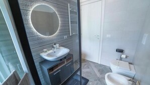 A modern bathroom with a glass-enclosed vanity, a round mirror, a toilet, and a bidet. - TaMo Lovely apartment (Fisciano)