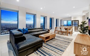 A modern living room with a black leather sofa, a wooden coffee table, and a dining area with a table and chairs. - Soul - 3 Bedroom SkyView Apartment - Q Stay (Surfers Paradise)