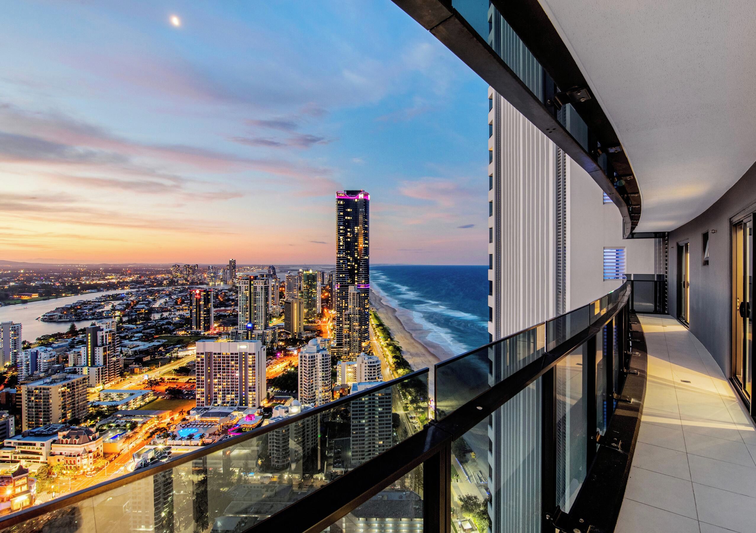 Een hoog hotel met een glazen balkon met uitzicht op een stadsbeeld, strand en oceaan.
