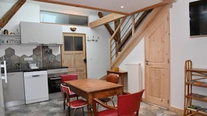 A kitchen with a wooden table and chairs, a dishwasher, and a wooden staircase. - Eco-friendly apartment in 15th century building, heart of Conflans (Albertville)