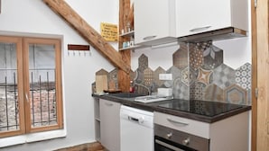 A compact kitchen with a dishwasher, oven, and a window with a view of a brick wall. - Eco-friendly apartment in 15th century building, heart of Conflans (Albertville)