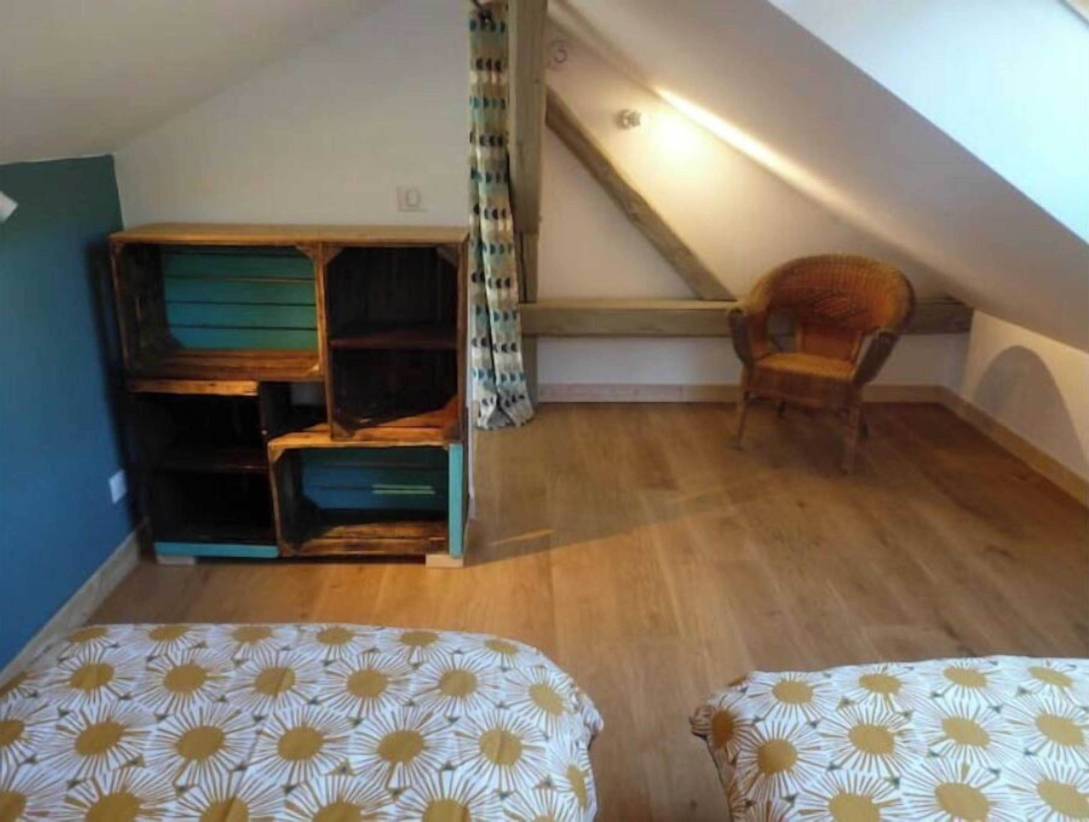 Ett litet vindsrum med ett sluttande tak, trägolv, en våningssäng med ett mönstrat överkast, en stol och en trappa som leder upp till en övre våning.