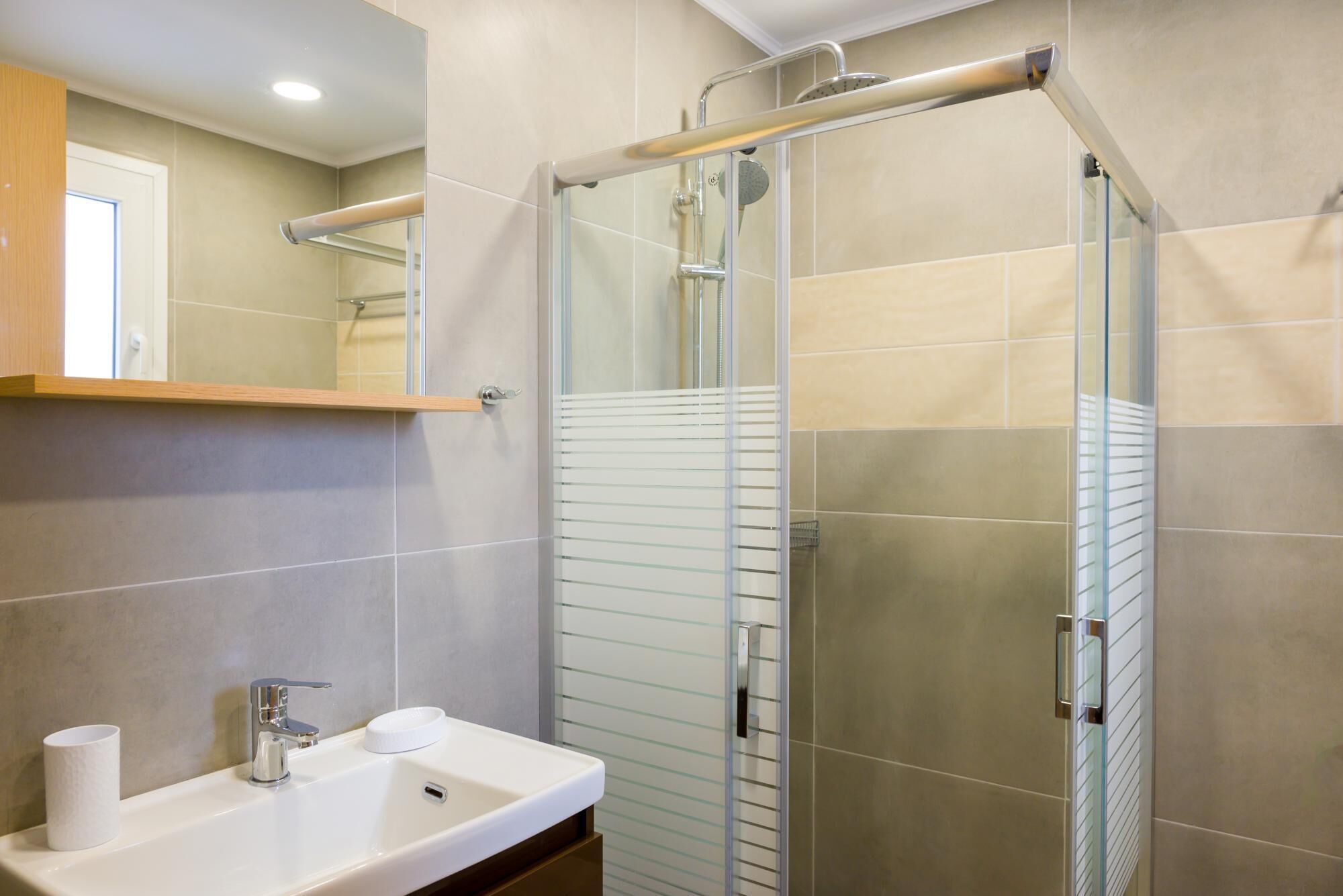 A modern bathroom with a glass shower enclosure, a sink with a mirror above, and a towel rack.