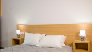 Una cama bien hecha con colcha color beige, dos mesitas de noche con lámparas y un cabecero de madera.