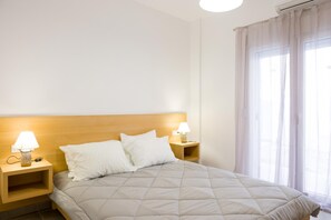 A neatly made bed with a wooden headboard, two bedside tables with lamps, and a large window with sheer curtains.