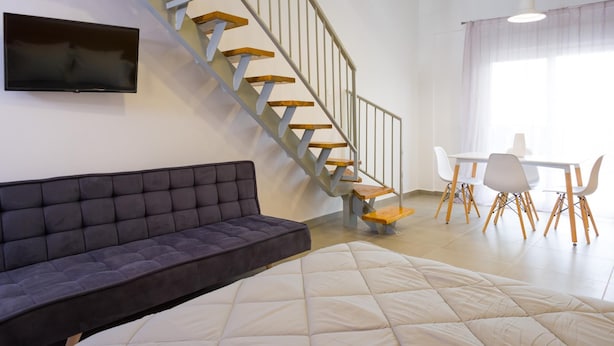 Een moderne woonkamer met een bank, een bed, een eethoek met stoelen en een trap.