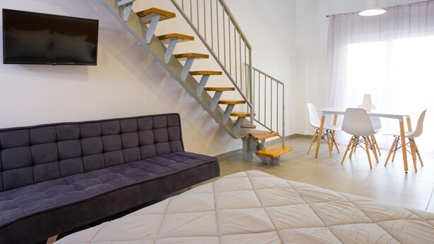 A modern living room with a sofa, a bed, a staircase, and a dining area. - Elounda Olithos Apartments 4 (Agios Nikolaos)