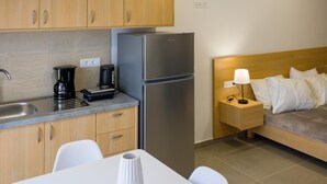 A modern kitchen with wooden cabinets, a stainless steel refrigerator, a coffee maker, and a dining table with a white vase. - Elounda Olithos Apartments 4 (Agios Nikolaos)