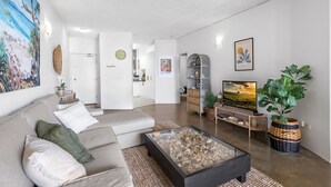 A modern living room with a sofa, coffee table, and a television. There are decorative items and a painting on the wall.