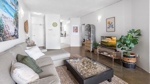 Ein modernes Wohnzimmer mit Sofa, Couchtisch und Fernseher. Dekorative Elemente und ein Gemälde sind an der Wand zu sehen.