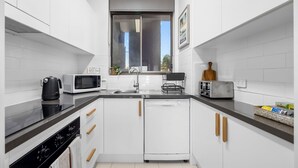 A compact kitchen with white cabinets, a black countertop, a microwave, a toaster, and a dishwasher.