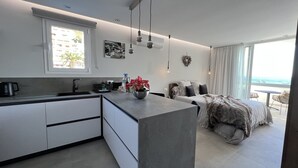 Eine moderne Küche mit Kochinsel, ein Essbereich mit Meerblick und ein Schlafzimmer mit großem Fenster.