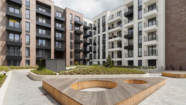 Un immeuble d’appartements moderne doté de nombreux balcons, d’un espace paysager central et d’un banc circulaire en bois.