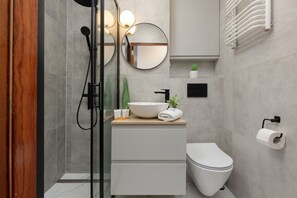 Un baño moderno con cabina de ducha de vidrio, un lavabo blanco con lavamanos, un inodoro y un espejo.