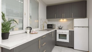 A modern kitchen with grey cabinets, a white countertop, a microwave, an oven, and a refrigerator.