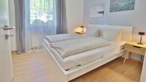 Makuuhuone, jossa on sänky, kaksi yöpöytää, ikkuna, jossa on ohuet verhot, ja seinätaidetta.