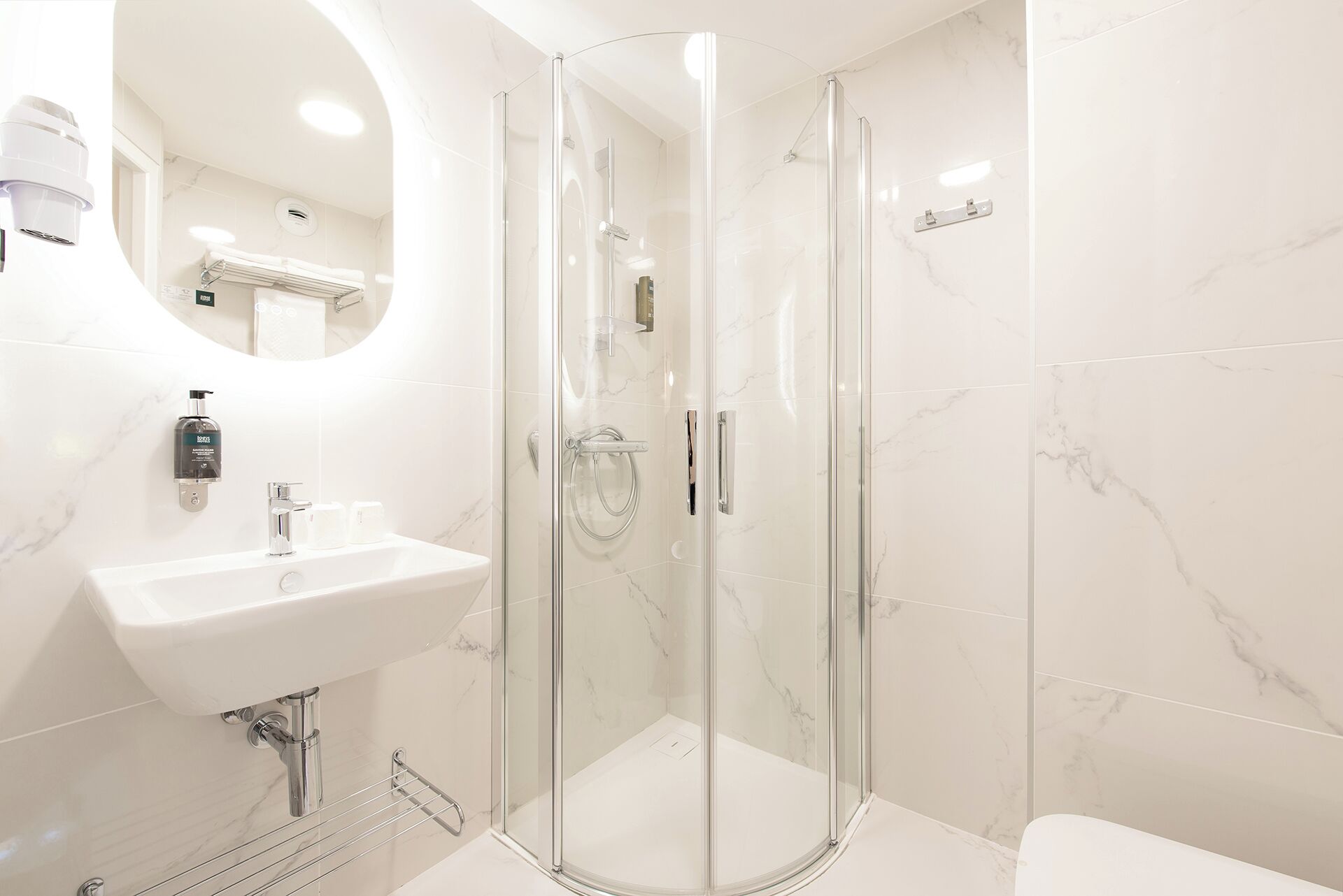A modern bathroom with a glass-enclosed shower, a white sink, and a marble-tiled wall.