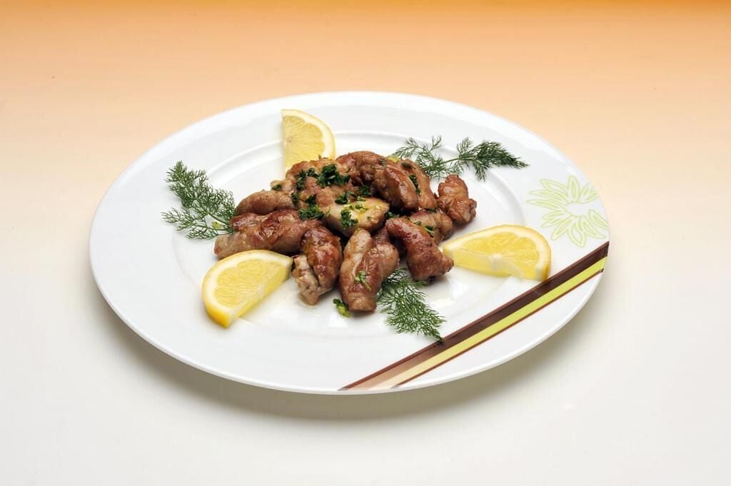 A plate of cooked meat garnished with herbs and lemon slices on a white plate with a floral design.