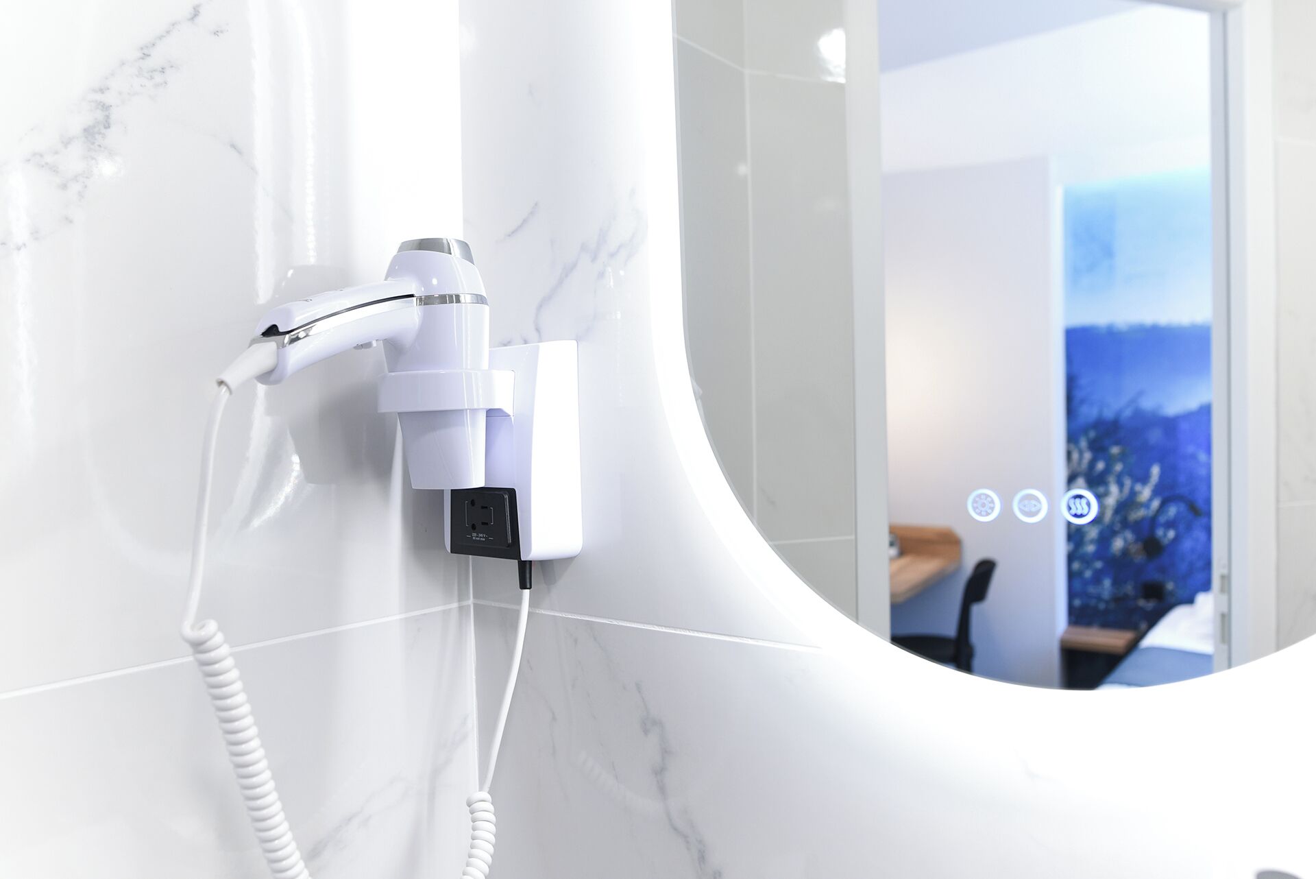 A modern bathroom with a white marble wall, a built-in hair dryer, and a visible power outlet.