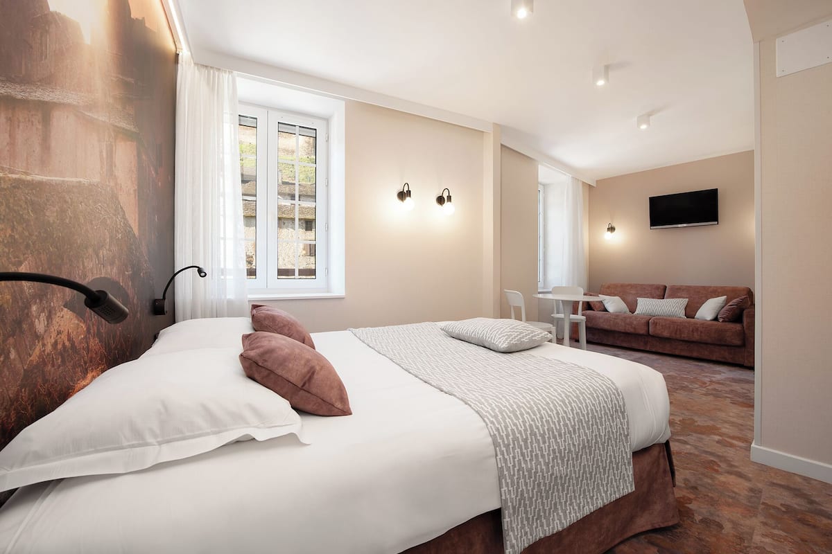 Et hotelværelse med en stor seng, et lille bord, en sofa og et fjernsyn ophængt på væggen.