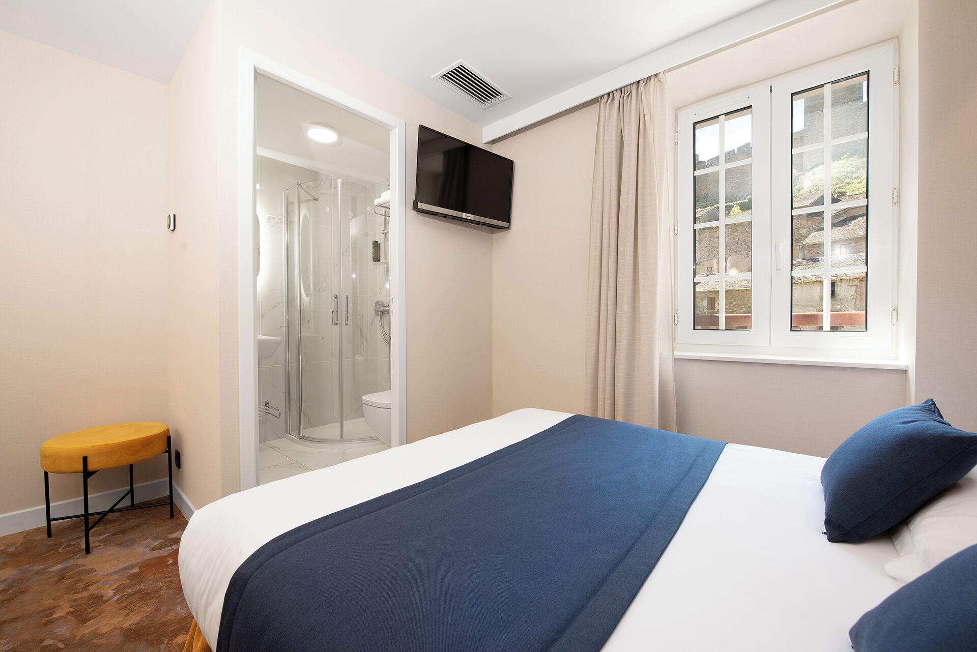 A bedroom with a bed, a TV, a window, and a shower area.