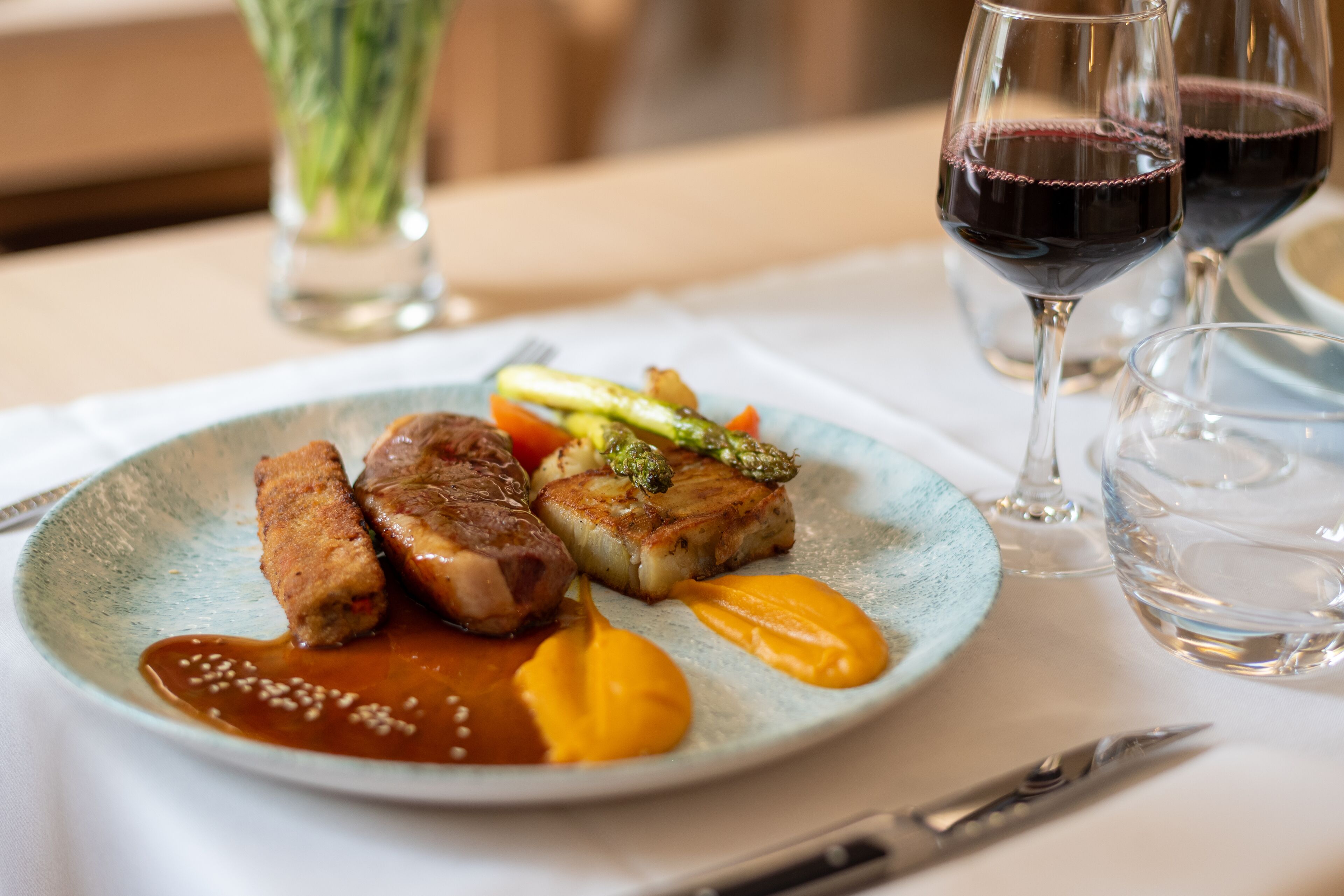 A plate of food with two pieces of meat, asparagus, and a sauce, accompanied by a glass of red wine.