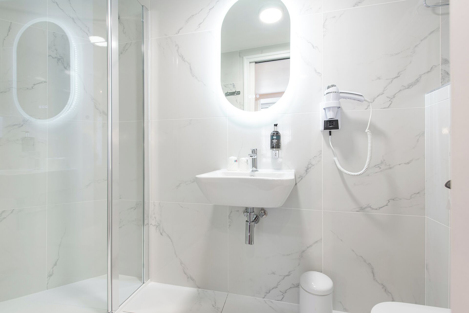A modern bathroom with a glass shower enclosure, a white sink with a handheld showerhead, and a toilet.