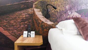 Un dormitorio con un mural de pared de piedra, una lámpara de noche, una mesita de noche de madera con un control remoto y una cama blanca.