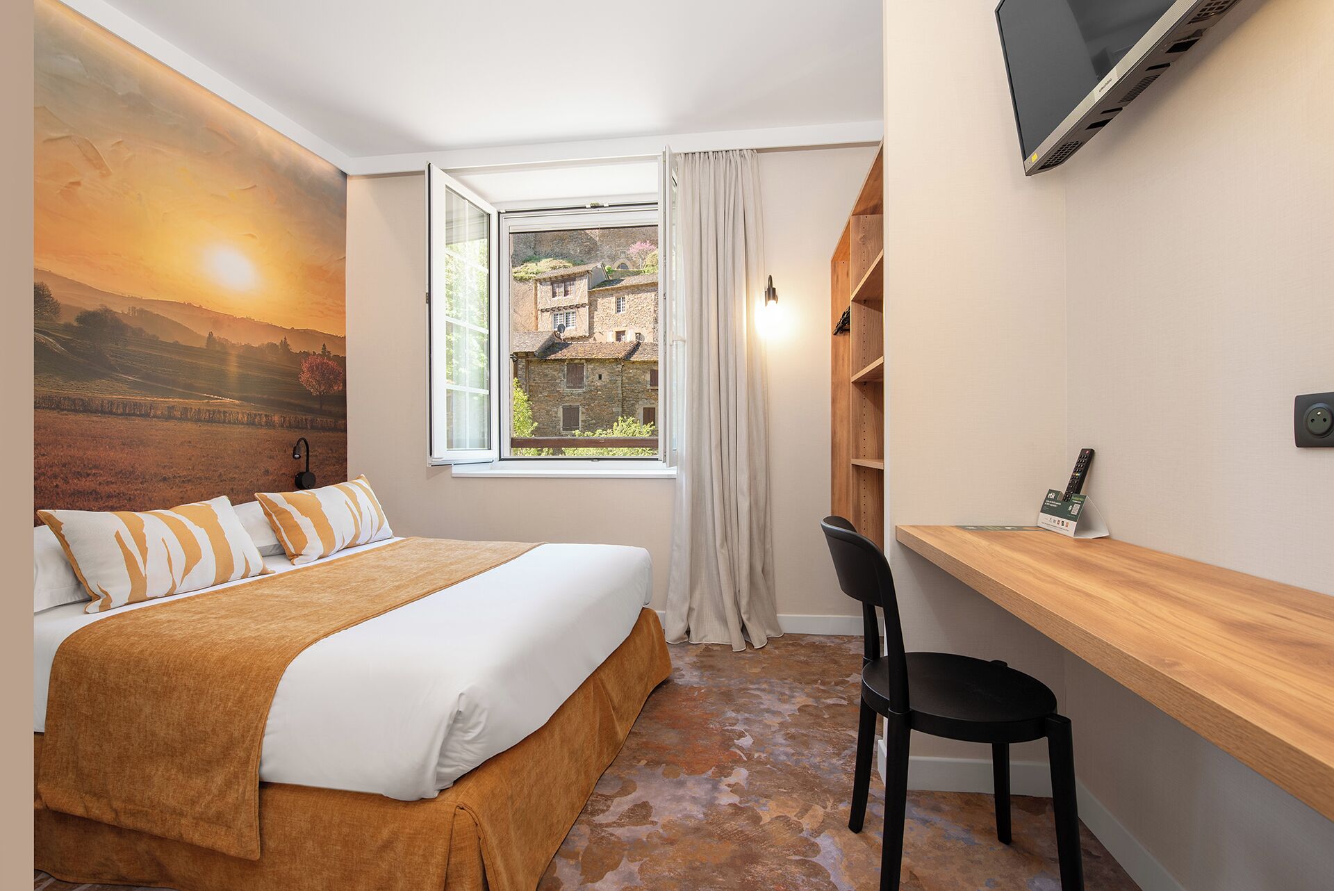Een slaapkamer met een bed, een bureau, een stoel, een televisie en een raam met uitzicht op een gebouw.