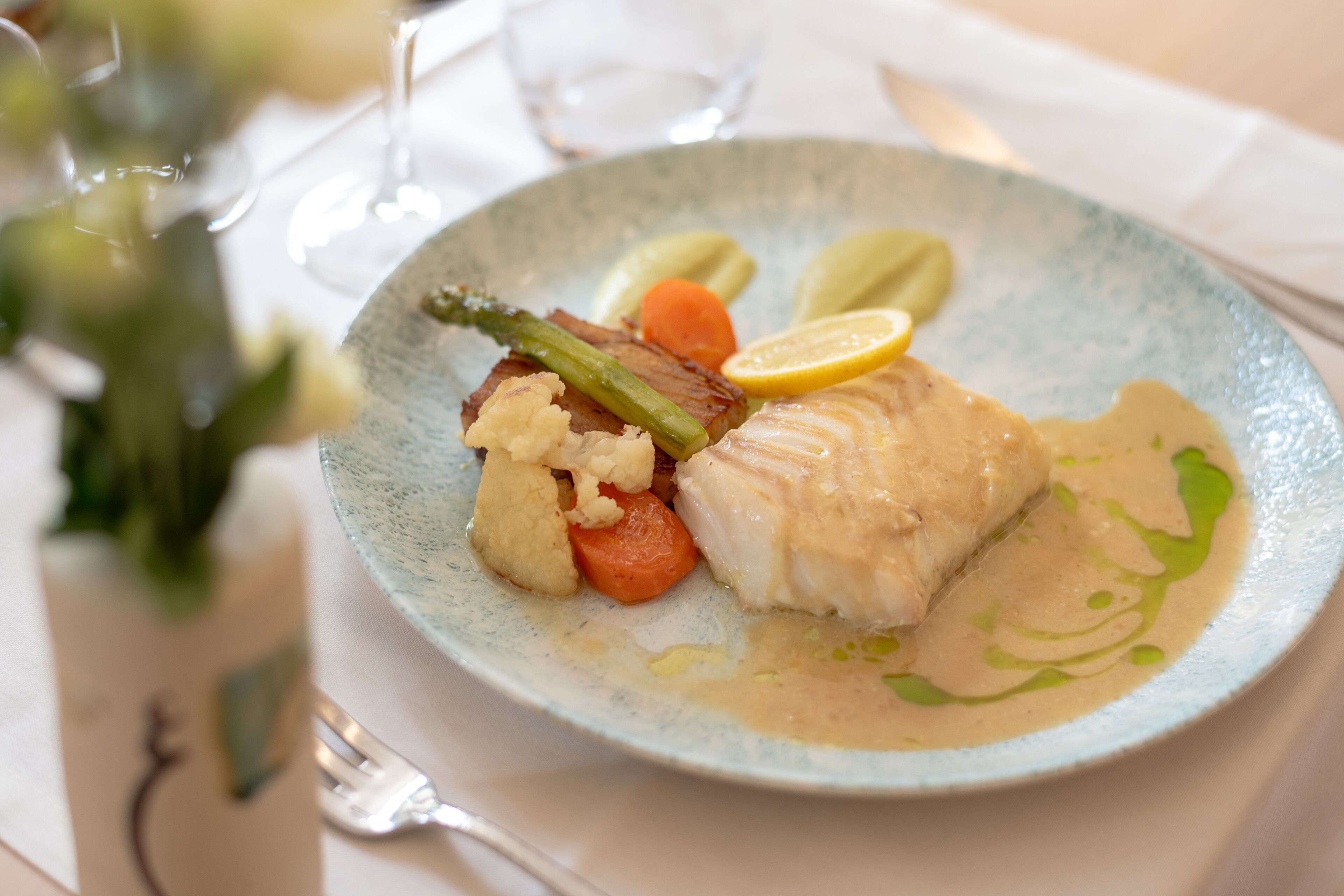 A plate of food with a piece of fish, vegetables, and a slice of lemon.