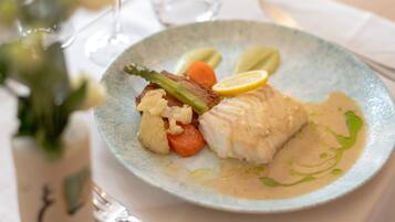 A plate of food with a piece of fish, vegetables, and a slice of lemon.