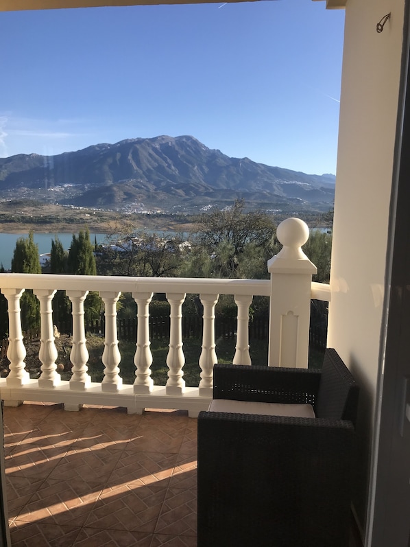 A balcony with a white balustrade overlooking a mountainous landscape and a body of water.