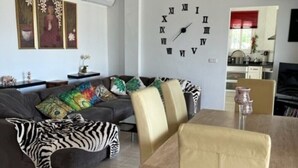 A living room with a sofa, a dining table with chairs, a zebra-patterned throw, and a wall clock. - Stunning Villa with a Private Pool, Panoramic views of Lake Vinuela (Los Romanes)