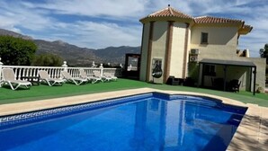 A swimming pool with a clear view of mountains in the background, a covered patio area, and a building with a tiled roof. - Stunning Villa with a Private Pool, Panoramic views of Lake Vinuela (Los Romanes)