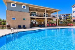 Ein Schwimmbad mit Liegestühlen, einer überdachten Terrasse und einem Backsteinhaus mit Balkonen.
