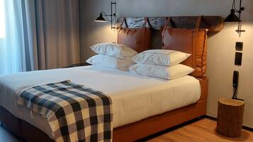 A neatly made bed with white linens and a checkered throw blanket. There are two wall-mounted lamps on either side of the bed.