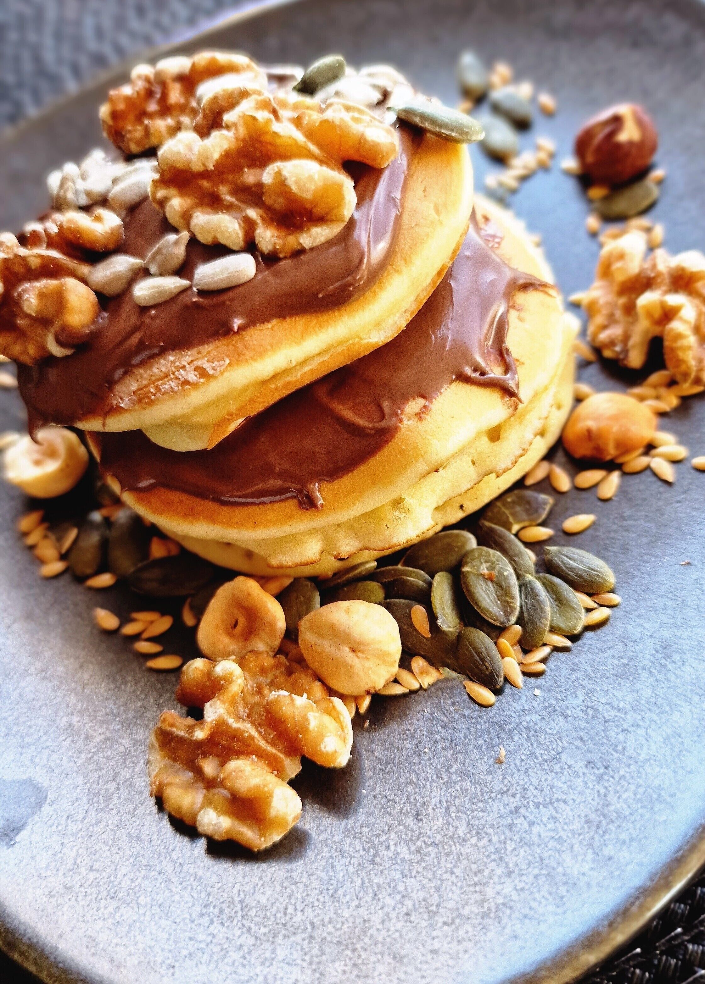 Uma pilha de panquecas com chocolate e nozes em um prato.