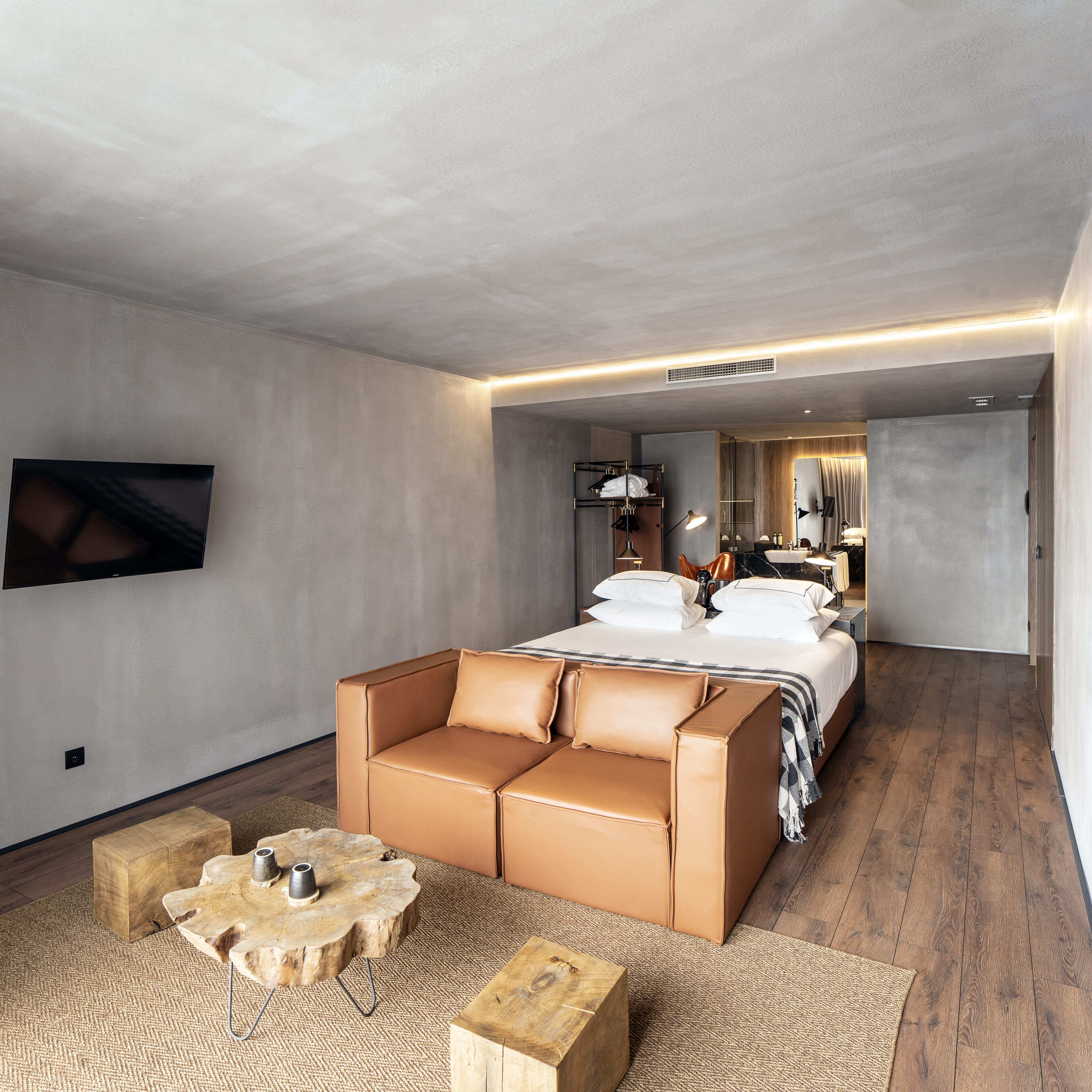Una habitación de hotel moderna con una cama grande, un sofá, una mesa de centro y un televisor montado en la pared.