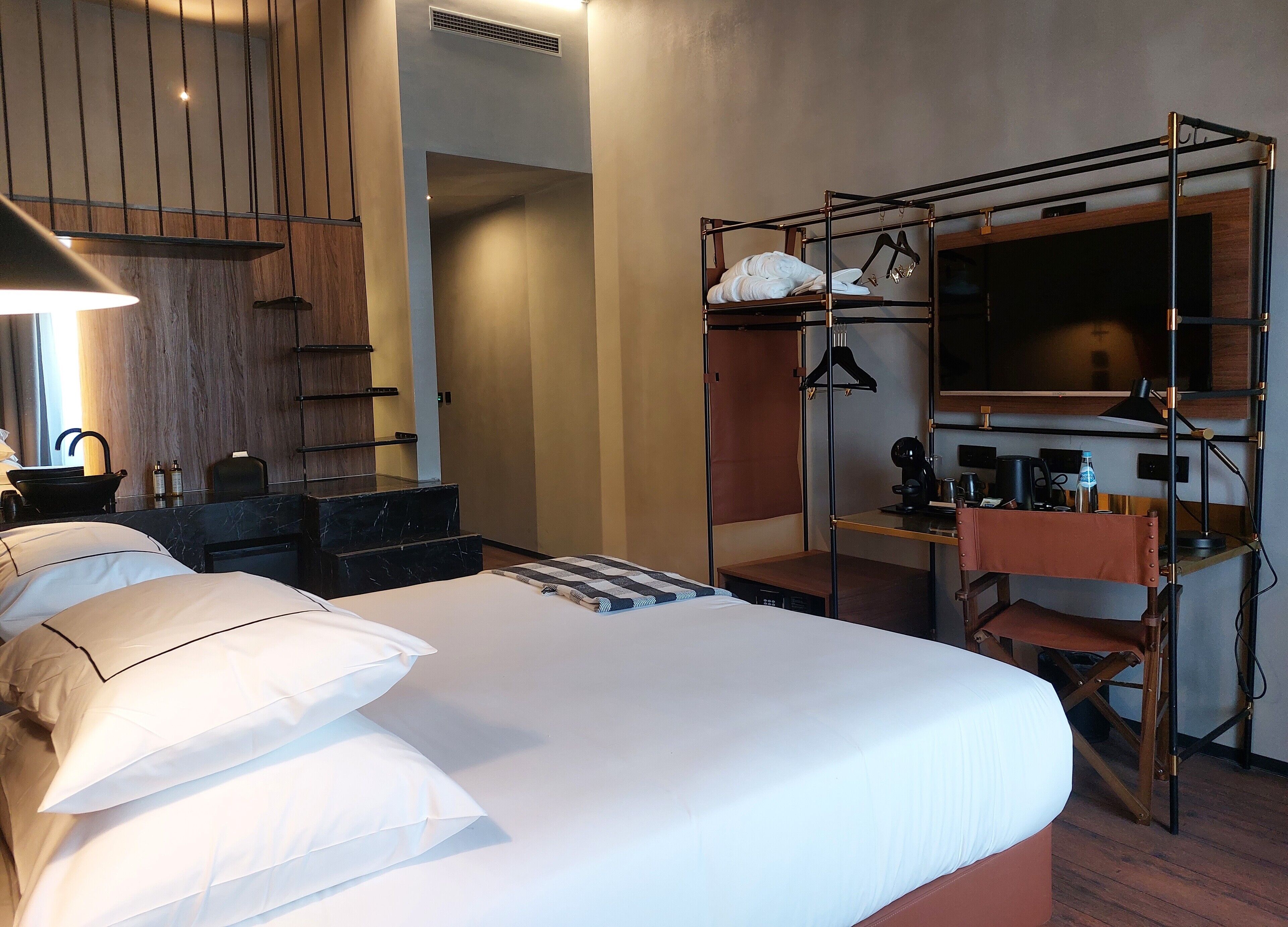 Una habitación de hotel con cama, escritorio, silla, armario, espejo y lavabo.