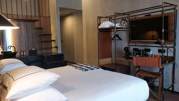 Una habitación de hotel con cama, escritorio, silla, armario, espejo y lavabo.