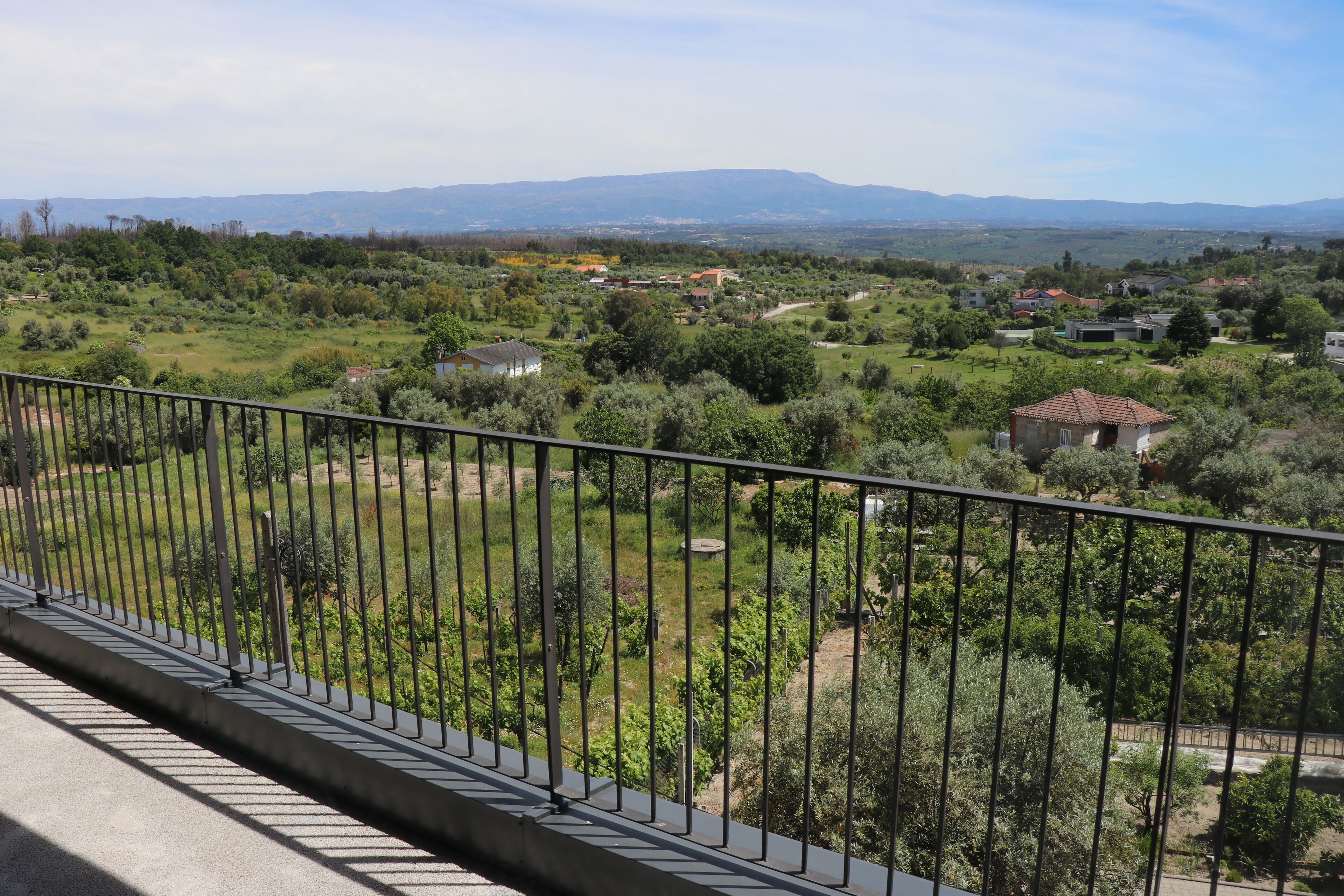 A balcony with a metal railing overlooking a rural landscape with houses and greenery.