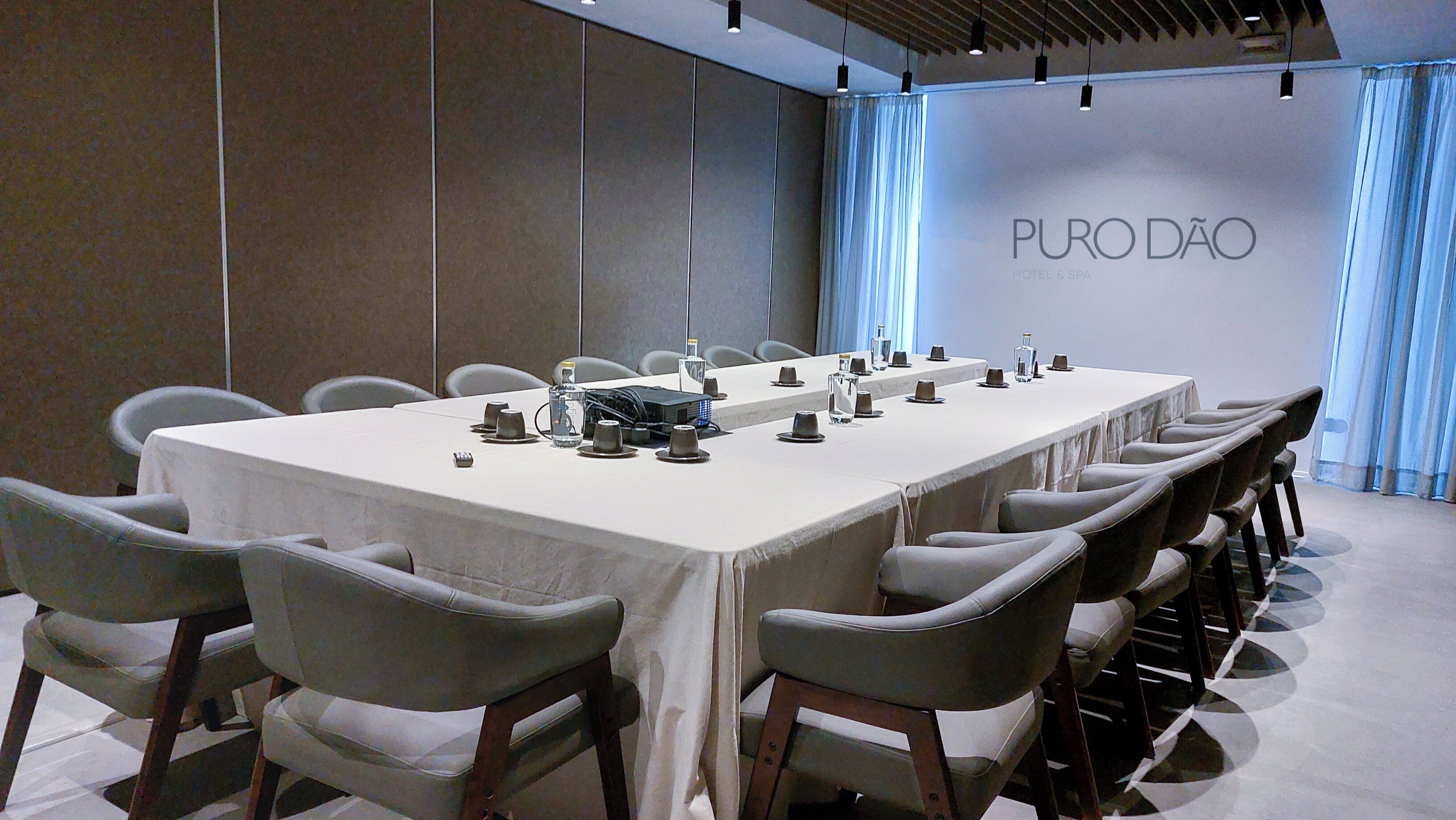 A conference room with a long table, chairs, a projector, and a wall with the text "PURO DÃO HOTEL & SPA".