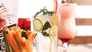 Ein Glas gekühltes Getränk mit Limette und Minze, eine Coca-Cola Dose und eine Schale mit Obstscheiben.