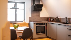Een moderne keuken met een inbouwoven, een zithoek met een tafel en stoelen, en een raam met natuurlijk licht.